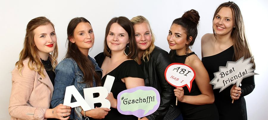 Sechs junge Frauen posieren ausgelassen mit Schildern beim Abiball